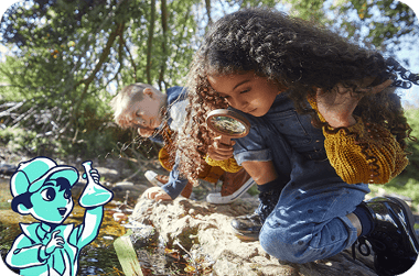 Two children kneel by a small stream outdoors, exploring the water with a magnifying glass, alongside an illustrated water scientist character.